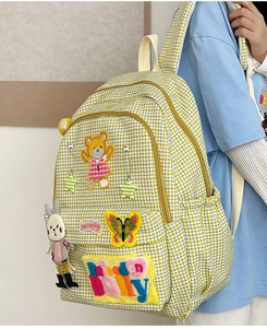 Detail view of yellow houndstooth backpack featuring cute cartoon embroidery and zip closure