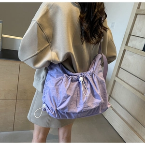 Close-up of a purple nylon drawstring crossbody bag worn by a model in casual style