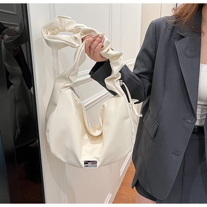 Close-up of off-white crescent bag featuring pleated strap and silver metal detail