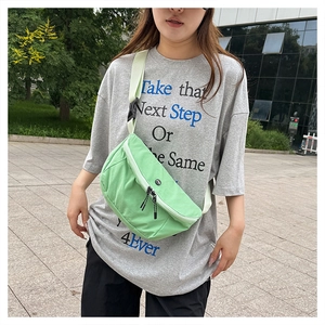 Outdoor shot of mint green nylon crossbody bag featuring double zippers and black strap