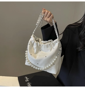 Detail of white quilted bucket bag with pearl chain and metallic woven handle