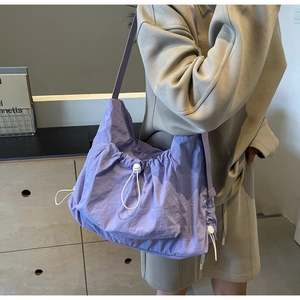 Detail of purple nylon crossbody bag with drawstring design worn by a female model