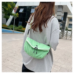 Detail view of mint green nylon crescent crossbody bag worn by a model in a city street