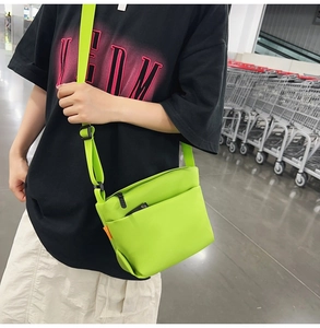 Fluorescent green nylon crossbody bag with adjustable strap worn by a model in a store