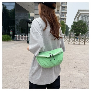Detail of mint green washed nylon crossbody bag with dual zippers on a gray outfit