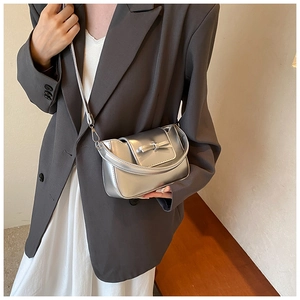Detail shot of a silver PU leather crossbody bag with bow accent on a model's shoulder