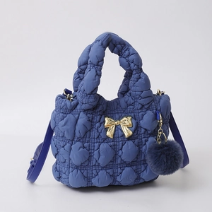 Vue détaillée du sac à main matelassé bleu foncé avec nœud doré et pompon en peluche doux