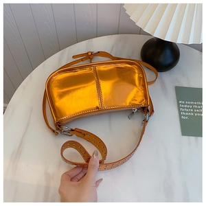 Détail du sac en cuir verni orange avec bandoulière large ornée de rivets argentés