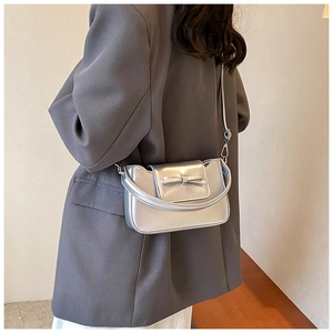 Silver metallic crossbody bag with bow detail worn over a grey blazer jacket