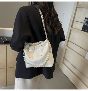 Detail of white quilted PU bucket bag with pearl strap and silver chain on model