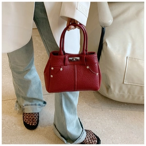 Detail der dunkelroten PU-Handtasche mit Lychee-Muster, silbernem Drehverschluss und Nieten