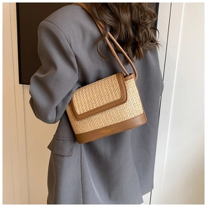 Sac à bandoulière en paille et cuir marron porté par un mannequin avec détail doré