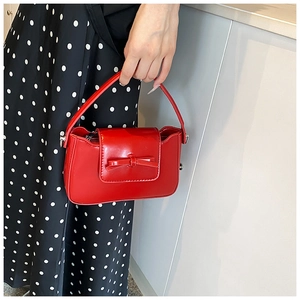 Close-up of a red mini handbag with a glossy finish and a 3D bow decoration on the front