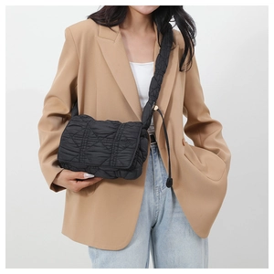 Detail of a black quilted puffer crossbody bag worn with a stylish blazer outfit