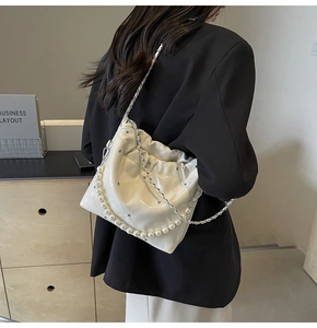 Detail of white quilted handbag featuring decorative pearl chain and metal strap