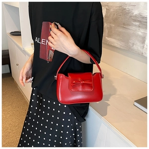 Detail view of a bright red glossy PU leather handbag featuring a stylish leather bow ornament