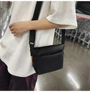 Detailed view of black matte cross-body bag with orange label on white waffle shirt