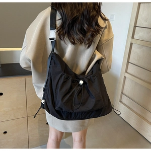 Detail of black nylon crossbody bag with drawstring closure and wide strap on model back