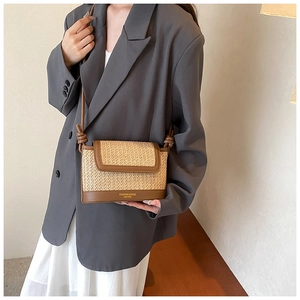 Détail d'un sac bandoulière en paille tissée avec garniture en cuir brun et sangle nouée