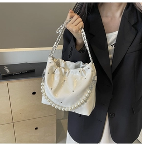 Detail of white quilted patent leather bucket bag with pearl chain and silver studs