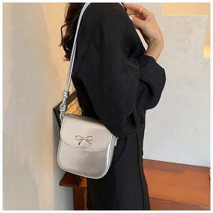 Detail of silver metallic saddle bag featuring a bow buckle and knotted shoulder strap