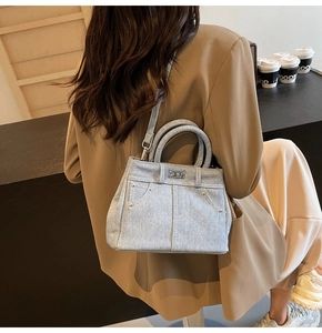 Détail du sac à main en denim bleu clair avec boucles argentées porté à l'épaule