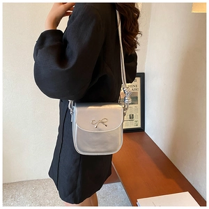 Close-up of a metallic silver crossbody bag with a butterfly clasp and knot strap detail