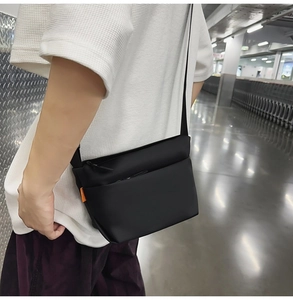 Detail view of black minimalist crossbody bag featuring orange label and zipper pockets