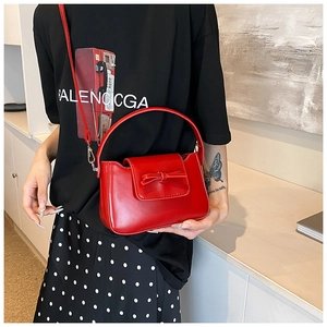 Detail of red PU leather handbag with bow decoration worn as a crossbody bag by model