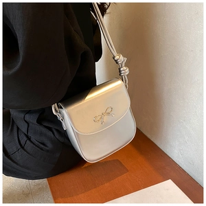 Detail of silver metallic PU crossbody bag featuring a delicate metal bow and knotted strap