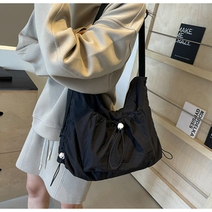 Detail view of black nylon crossbody bag featuring drawstring design and wide shoulder strap