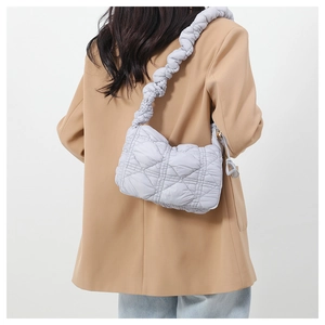 Detail of light blue quilted nylon shoulder bag with wide pleated strap on female model