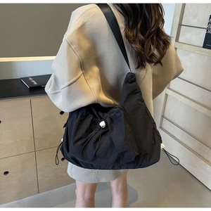 Detail of black nylon crossbody bag featuring drawstring texture and white orb buckle
