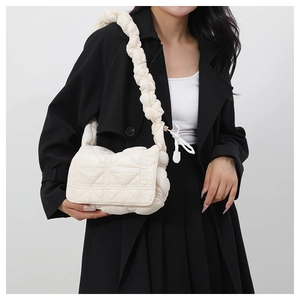 Detail of quilted puffy crossbody bag with ruffled strap worn by model in black coat