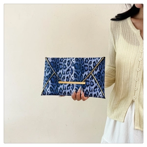 Blue leopard print envelope clutch bag with gold metallic trim held by a model
