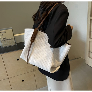 Detail view of the white woven tote bag texture with brown leather strap on a shoulder