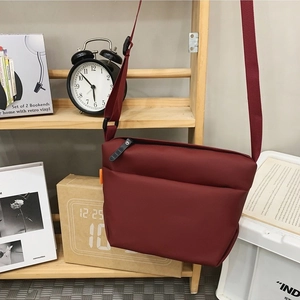 Minimalist burgundy red crossbody bag made of sleek fabric on a wooden shelf display