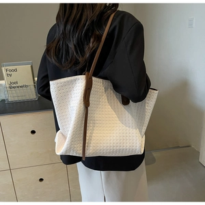 Detail of white woven tote bag featuring brown leather shoulder straps and large capacity