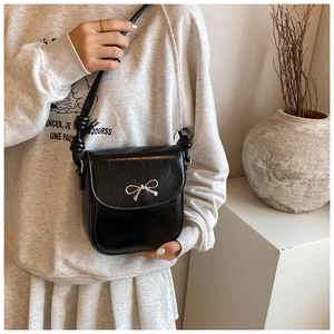 Detail of black glossy leather saddle bag with silver bow hardware and knotted strap