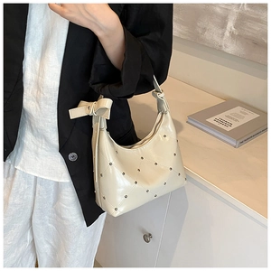 Détail du sac bandoulière beige matelassé avec clous argentés et nœud décoratif