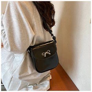 Detail of a black PU leather crossbody bag with a silver metallic bow and knotted strap