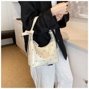 Détail du sac baguette en cuir PU crème avec rivets matelassés et bandoulière nouée
