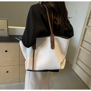 Detail of white woven tote bag with brown leather shoulder straps in a modern interior