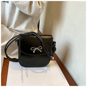 Detail of glossy patent leather crossbody bag with a silver bow knot buckle ornament