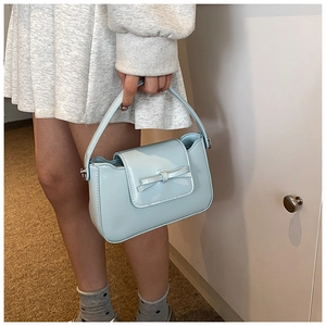 Detail shot of light blue PU leather handbag featuring a matching bow and metal D-rings