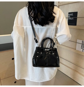 Détail d'un sac bandoulière en cuir verni noir avec fermoir rotatif argenté et rivets