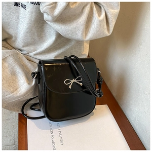 Detailed macro shot of black patent leather crossbody bag with silver metal bow accent