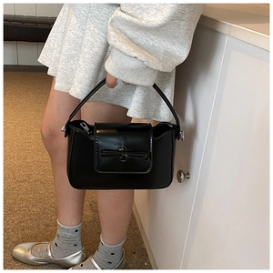 Detail shot of black PU leather handbag with a stylish bow decoration and smooth finish