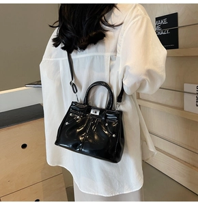Détail d'un sac à bandoulière en cuir verni noir avec boucle porté par un mannequin
