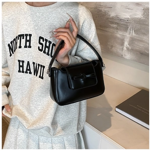 Detail of a black faux leather handbag with a bow decoration and a smooth glossy finish